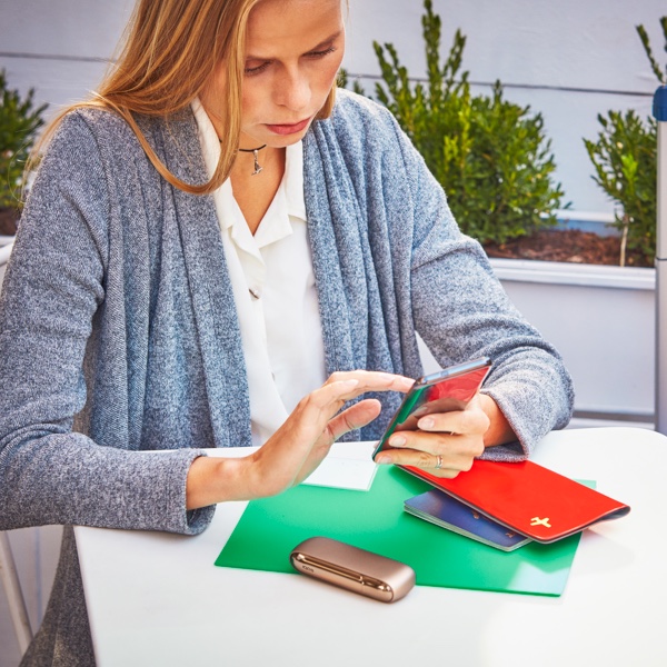 A woman using a mobile phone; her passport and IQOS device nearby.